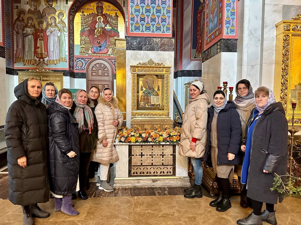 Группа флористов у иконы, украшенной оранжевыми и жёлтыми цветами