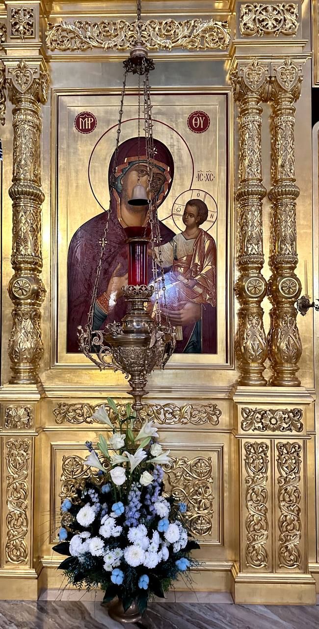 Бело-голубая цветочная композиция у иконы Богородицы в золочёном киоте