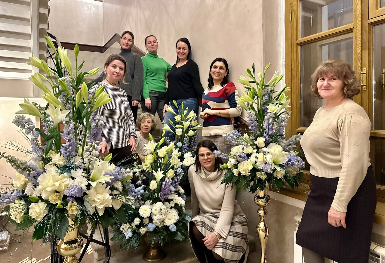 Участницы курса рядом с готовыми композициями из белых лилий и голубых цветов